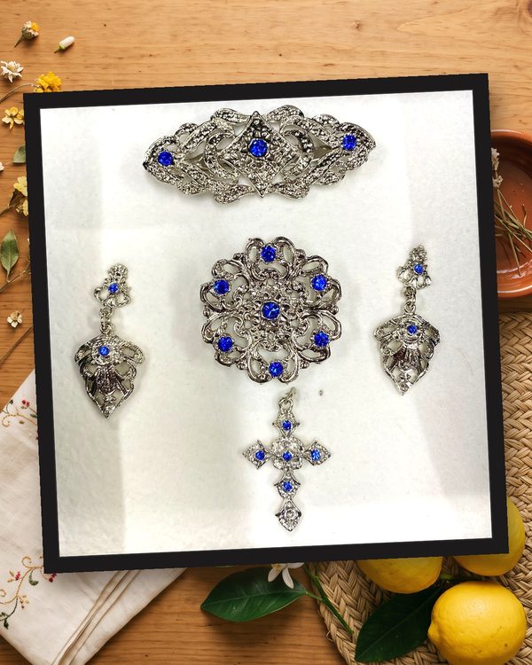 Aderezo plata y azul: pendientes largos, broche redondo, pasador para el pelo y cruz, en metal plateado brillante con cristales azules.