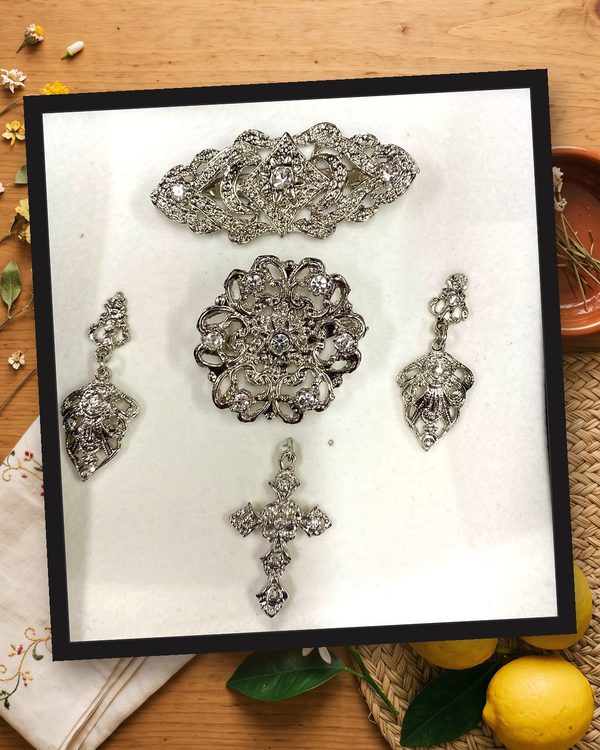 Aderezo plata y cristal: pendientes largos, broche redondo, pasador para el pelo y cruz, en metal plateado con cristales transparentes.