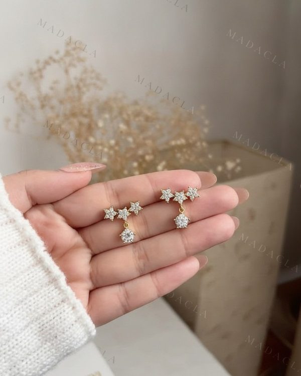 Pendientes dorados con tres estrellas y una piedra redonda colgante. Todas las figuras presentan incrustaciones de piedras transparentes.
