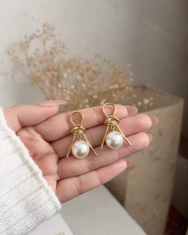 Pendientes dorados con una estructura geométrica. Presentan un nudo superior y de ellos cuelga una perla esférica de color blanco nacarado.