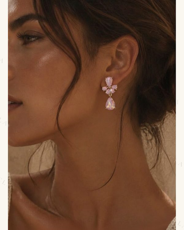 Pendientes colgantes dorados con piedras facetadas rosas en la parte superior y una lágrima iridiscente en la inferior.