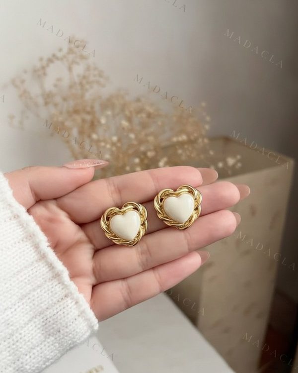 Pendientes de botón con corazón en blanco cremoso, enmarcados por un borde trenzado de color dorado.