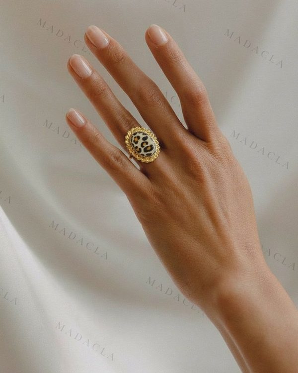 Anillo de color dorado con adorno central ovalado de estampado animal, tipo leopardo, y borde trenzado.