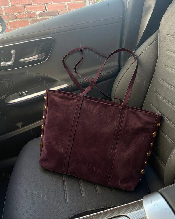 Bolso tote color burdeos con apariencia de ante, asas finas y tachuelas doradas en los laterales.