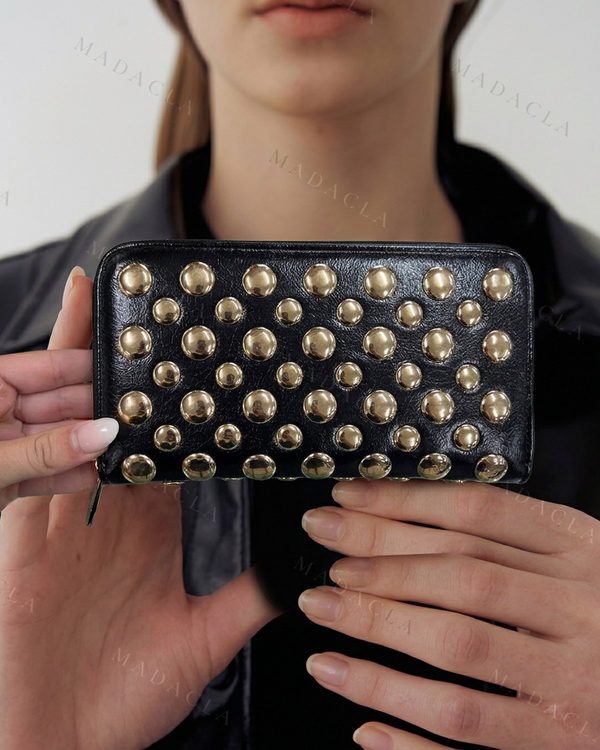 Monedero rectangular negro con cierre de cremallera lateral. Adornado con tachuelas metálicas redondas doradas de varios tamaños.