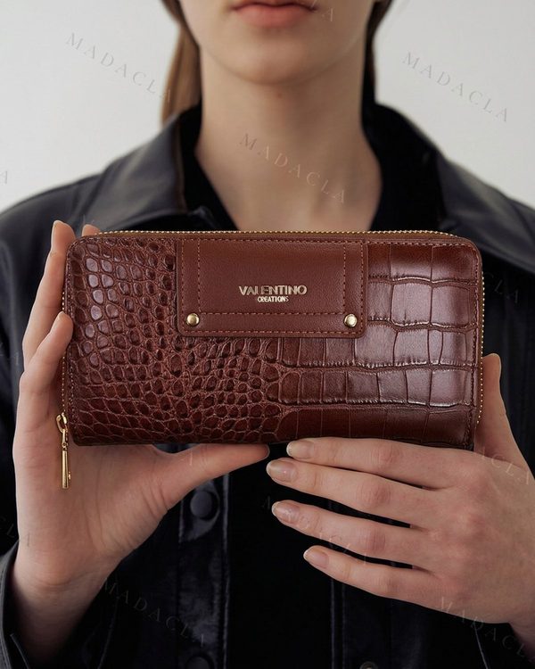 Monedero marrón con grabado de cocodrilo y cremallera dorada. En el frontal destaca Valentino Creations con remaches dorados.