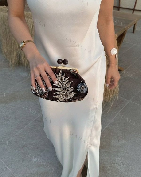 Bolso de mano de terciopelo oscuro con broche de dos bolas y bordados metálicos de hojas y motivos florales en tonos azules.