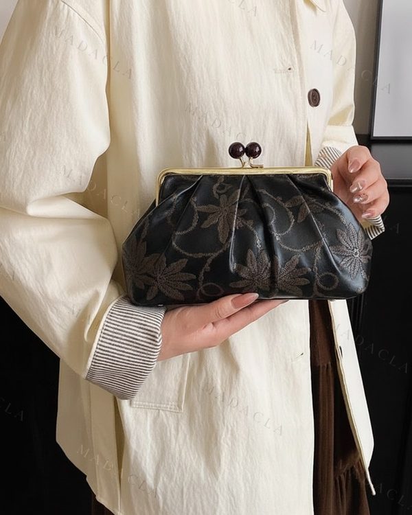 Bolso de mano negro con estampado de flores marrones, cierre metálico dorado de boquilla con dos bolas oscuras y pliegues fruncidos en la parte superior.