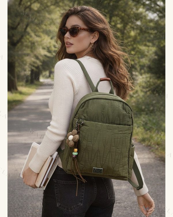 Mochila verde militar con costuras acolchadas en zigzag, asa superior de mano, tirantes ajustables, bolsillo frontal con cremallera y llavero decorativo de flor colgante.