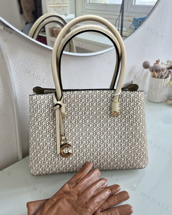 Bolso tote estructurado beige con estampado de letras marrones. Tiene asas rígidas y un adorno colgante dorado.