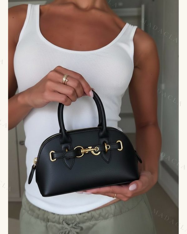 Bolso negro con textura, forma de cúpula y cierre de cremallera dorada. Asas superiores y adorno central también dorados.