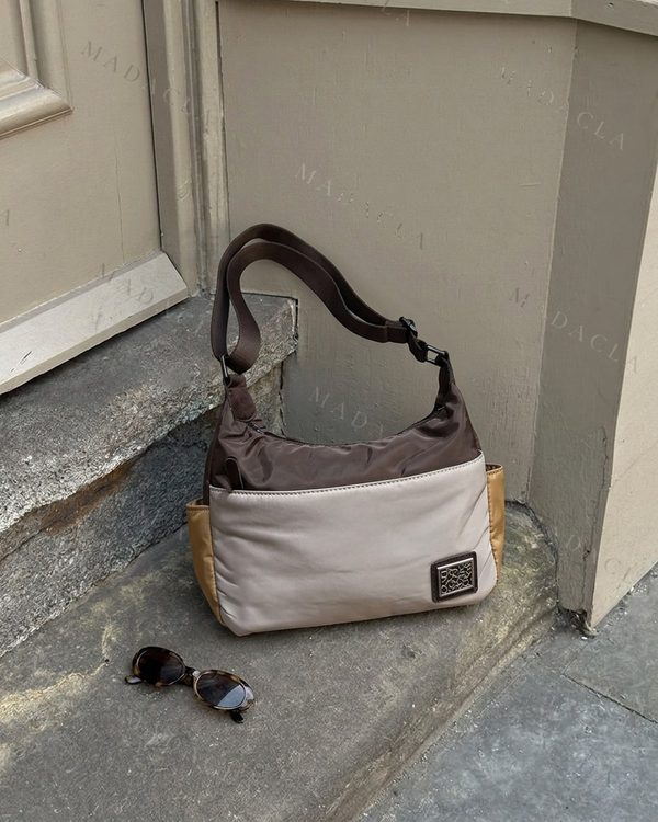 Bolso de hombro en marrones, beige y ocre. Tejido aparente suave, con correa ajustable y detalle metálico frontal.