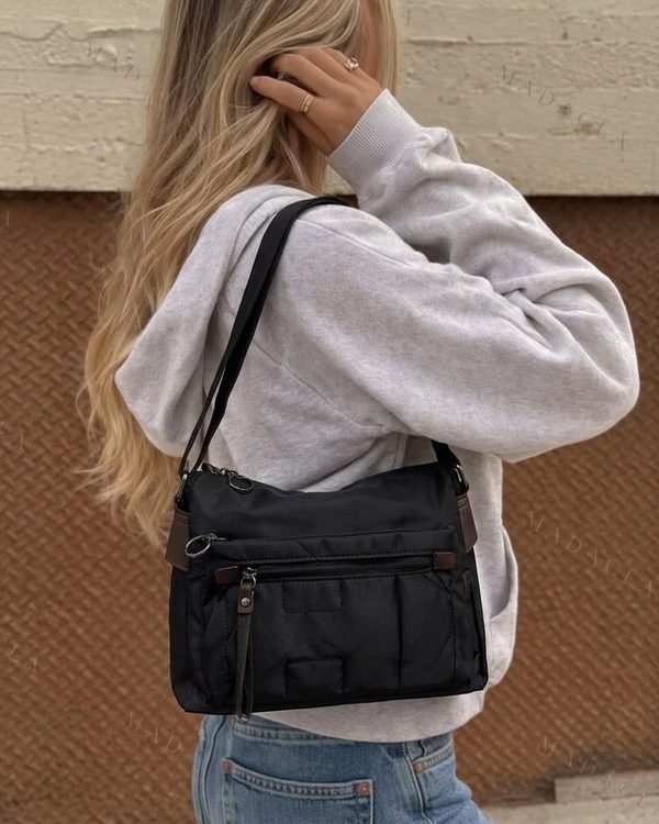 Bolso bandolera negro de tejido acolchado, con correa ajustable. Dispone de varios bolsillos exteriores con cremallera y detalles en tono marrón.