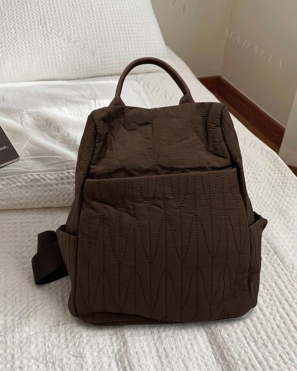 Mochila marrón oscuro de tejido acolchado con patrón de costuras verticales. Incluye bolsillo frontal, laterales y asa superior.