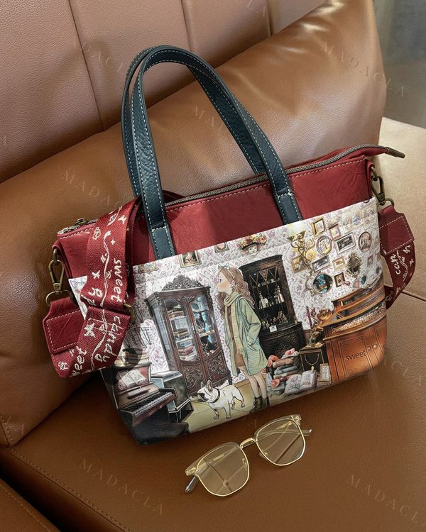Bolso tote rojo y negro con asas superiores y bandolera. Destaca su estampado frontal ilustrado y cierre de cremallera.