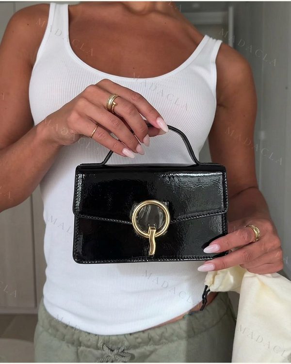 Bolso de mano rectangular negro, con acabado brillante y asa superior. Cierre de solapa con adorno metálico dorado.