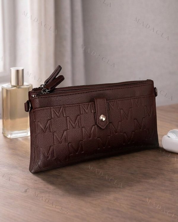 Cartera de mano marrón oscuro con textura de piel y patrón de letras M en relieve. Cierre de cremallera y solapa con botón metálico.