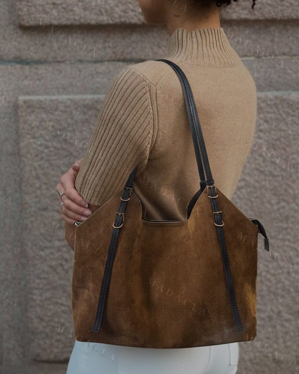 Bolso tote de piel vuelta marrón tostado con asas negras. Presenta tiras laterales decorativas, hebillas doradas y una tira trenzada.