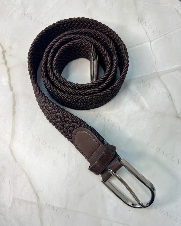 Cinturón de goma unisex en marrón oscuro, con tejido trenzado elástico. Presenta hebilla metálica plateada y detalles de puntera y presilla marrones.