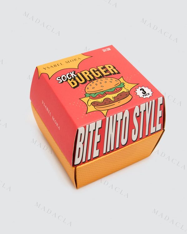 Pack de calcetines en caja de hamburguesa: tres pares con estampados variados, de lunares blancos, rodajas rojas con formas verdes y un dibujo de marrones y amarillos. Van juntos, en su caja.