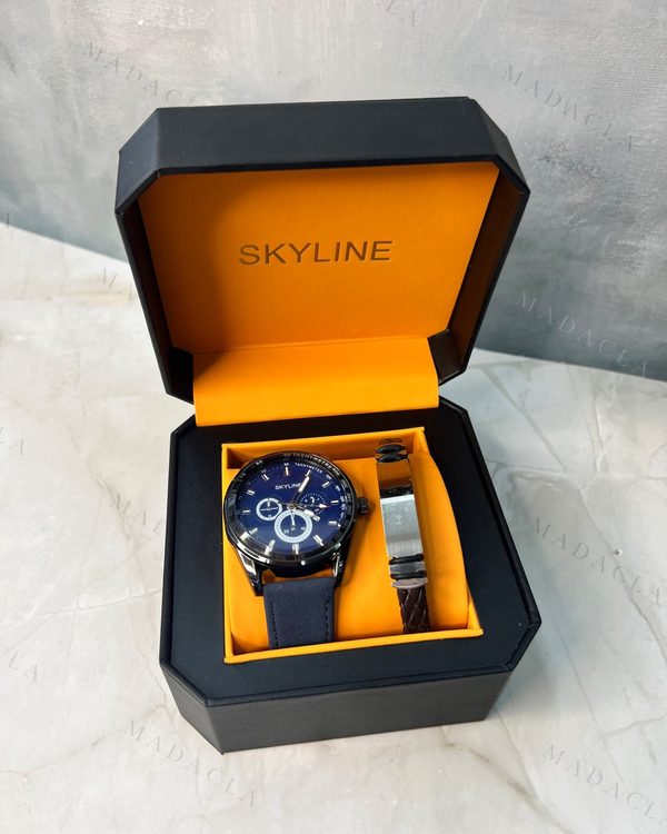 Pack de regalo en caja negra SKYLINE con interior naranja. Incluye reloj de esfera azul oscuro, correa azul, y pulsera trenzada marrón con placa plateada.