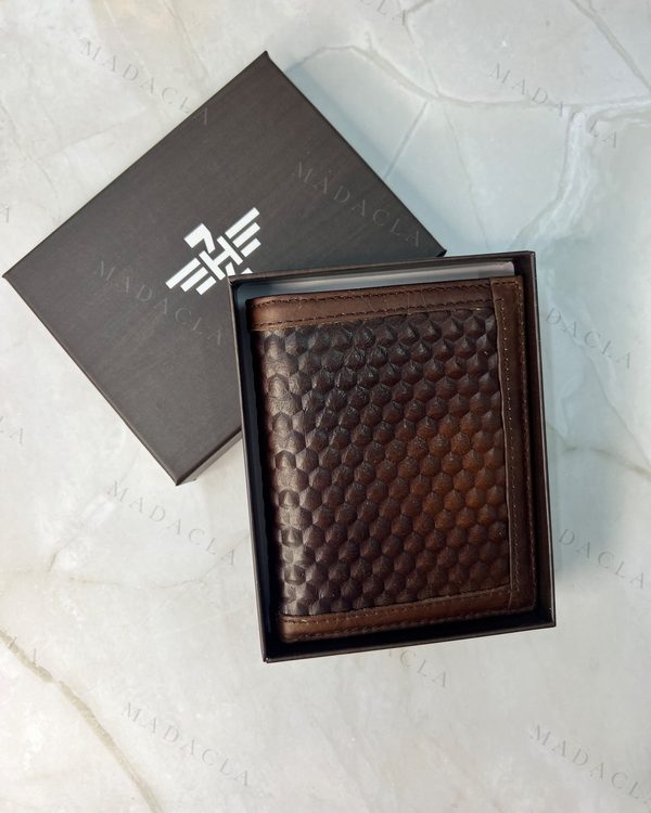 Cartera de hombre plegable en tono marrón oscuro. Presenta textura hexagonal en relieve y bordes lisos. Lleva grabado MADACLA en su caja.