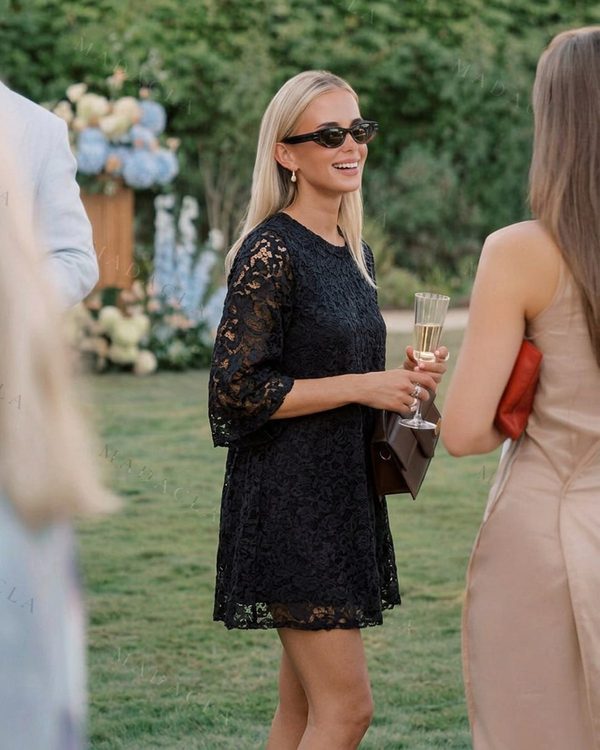 Vestido corto negro de encaje con corte recto y escote redondo. Las mangas son tres cuartos y el bajo tiene remate de encaje.