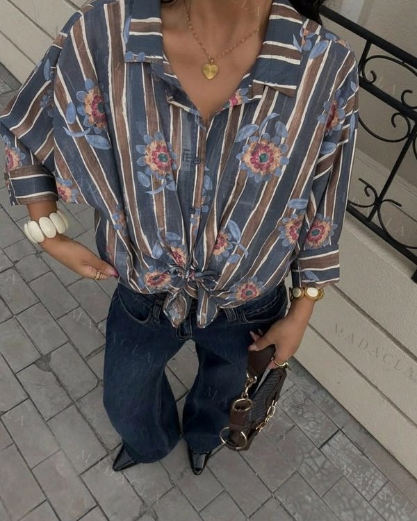 Camisa de tejido ligero con estampado de rayas azules, marrones y blancas, y flores. Cuello camisero, mangas largas remangadas, botones frontales; anudada a la cintura.