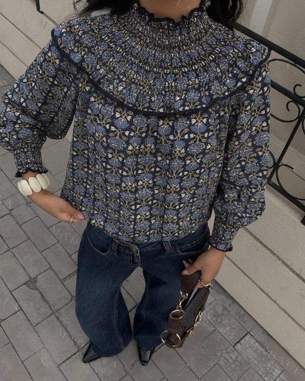 Camisa de flores en tonos azules con cuello alto y puños fruncidos. Presenta volantes decorativos con ribete oscuro.