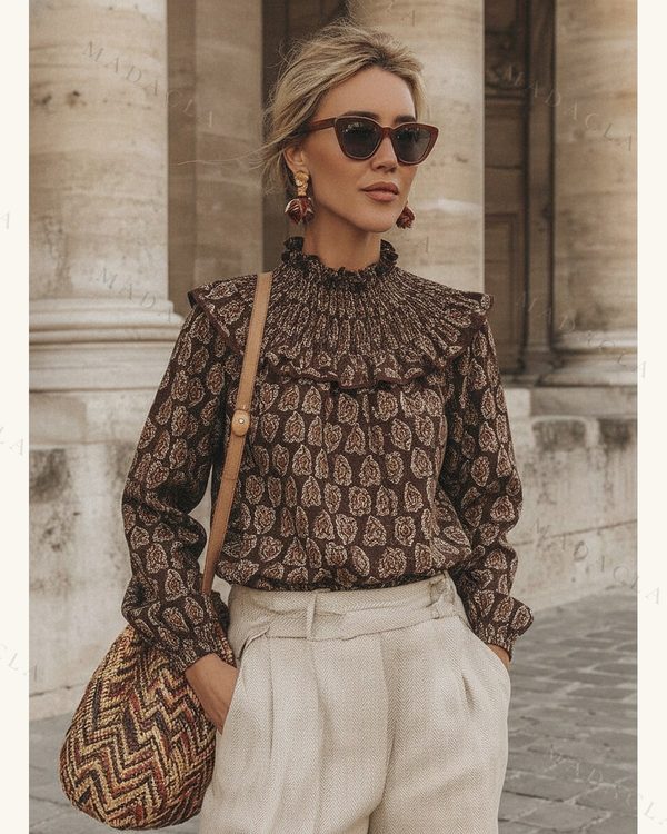 Camisa de tejido estampado marrón con cuello alto fruncido, volantes y mangas largas abullonadas con puño elástico.