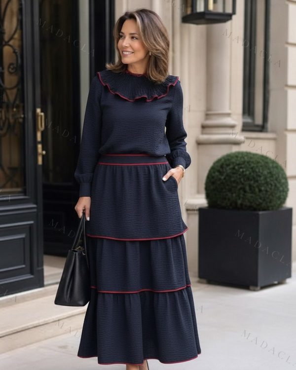 Conjunto azul marino de tejido texturizado. Blusa de manga larga con cuello de volante fruncido y ribete rojo. Falda larga escalonada con el mismo ribete.
