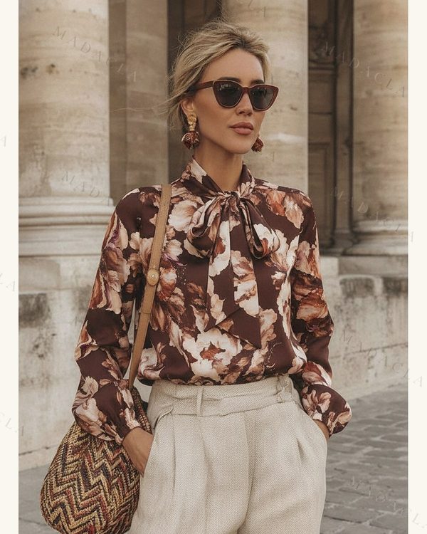 Camisa de tejido satinado marrón con estampado floral crema y tostado. Cuello con lazada y mangas largas, abullonadas en el puño.
