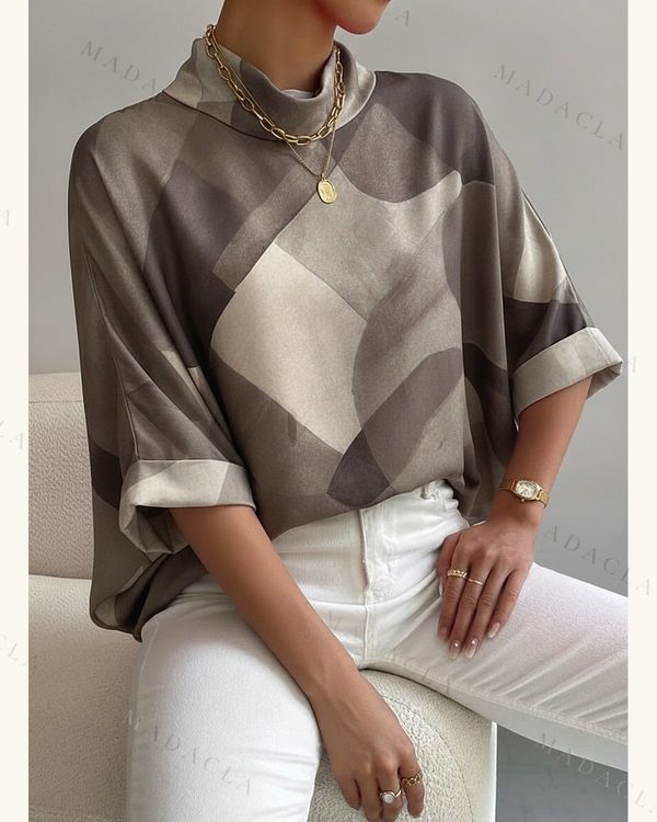 Camisa de tejido con caída y brillo, con estampado geométrico en tonos grises, marrones y crema. Presenta cuello alto y mangas amplias con vuelta.