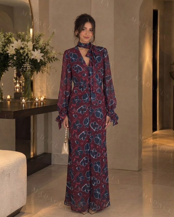 Vestido largo y fluido en burdeos con estampado floral azul y rosa. Escote en V con lazo al cuello y mangas largas con puños de lazada.