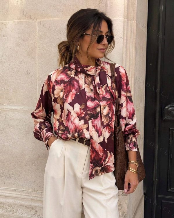 Camisa de tejido fluido con estampado floral burdeos y rosa. Destaca su cuello lazada y mangas largas con puños abotonados.