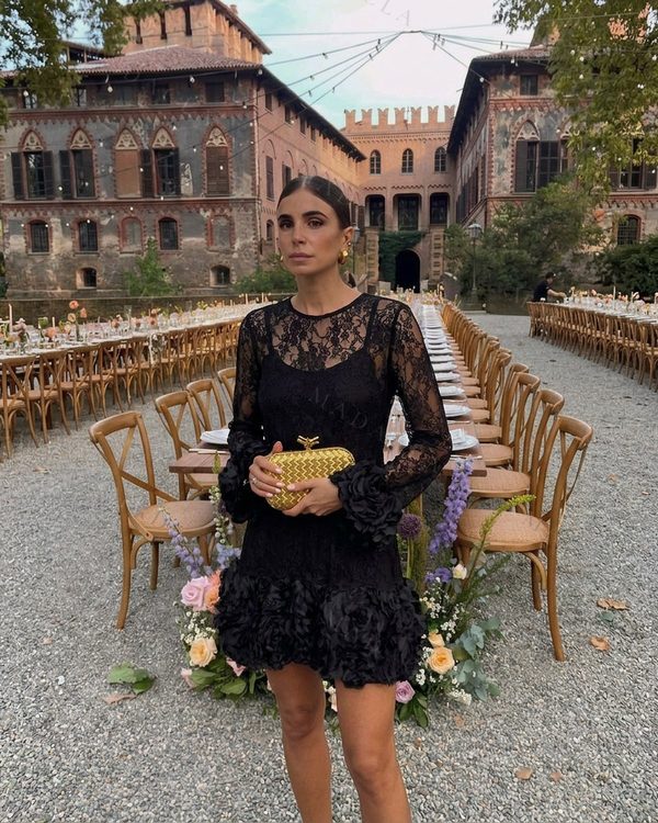 Vestido corto negro de encaje con escote redondo y mangas largas transparentes. Bajo y puños adornados con volantes de flores de tejido.