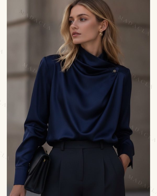 Blusa satinada azul marino de cuello alto drapeado, con un botón en el hombro y manga larga con puño abotonado. También la tenemos en marrón y champán.