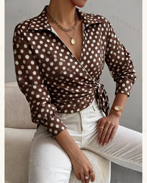 Blusa marrón con lunares blancos, de manga larga con puño y cuello de solapas. Es cruzada, con escote de pico y lazada lateral.