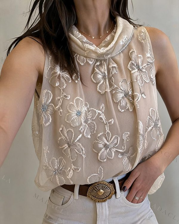 Blusa crema sin mangas de corte recto con cuello vuelto drapeado y bordados de flores brillantes en tono a juego. También la tenemos en morado, negro y marrón.