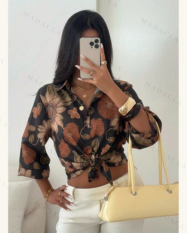 Blusa estampada oscura con motivos florales marrones, cuello camisero, manga tres cuartos y botones, anudada a la cintura. Pantalón claro, collar, anillos, pulseras y bolso amarillo. Se venden por separado.