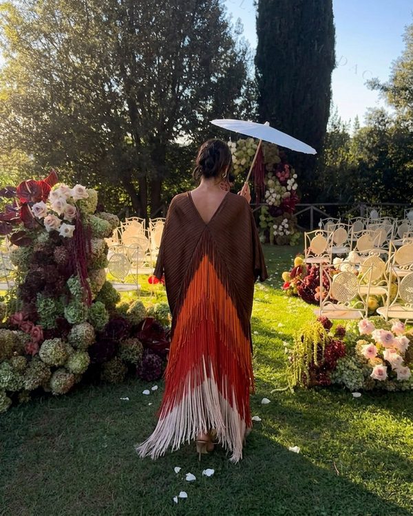 Vestido largo y holgado de cuerpo plegado marrón con escote en pico trasero. La falda lleva flecos en degradado naranja, rojo y crudo.