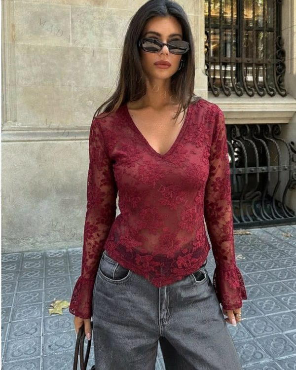 Camiseta burdeos de encaje calado floral. Presenta escote en pico, mangas largas con puños acampanados y bajo asimétrico de puntas.