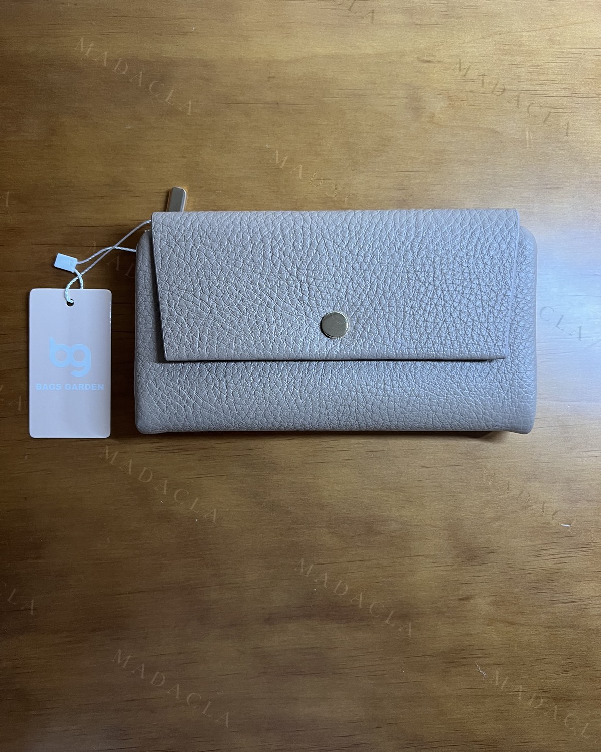 Cartera de piel granulada en gris claro, con solapa y cierre de botón plateado.