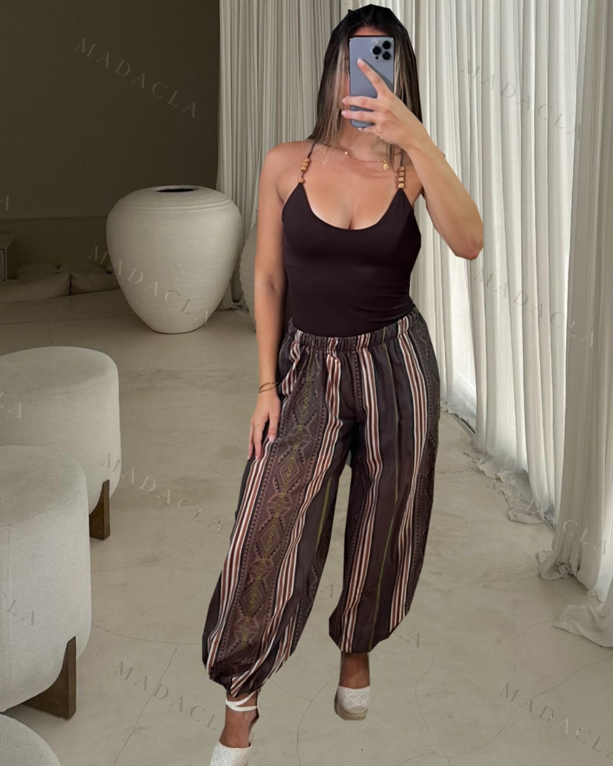 Top marrón oscuro de tejido liso con escote redondo y tirantes con abalorios. Pantalones largos y fluidos de corte ancho, con estampado de rayas y motivos geométricos en tonos tierra. Se venden por separado: puedes llevarte solo el que quieras, no hace falta el conjunto entero.